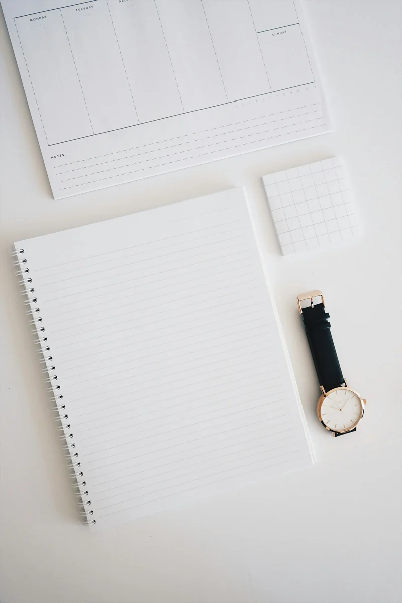 Open planner and notepad with a wristwatch on a white desk (demo photo)