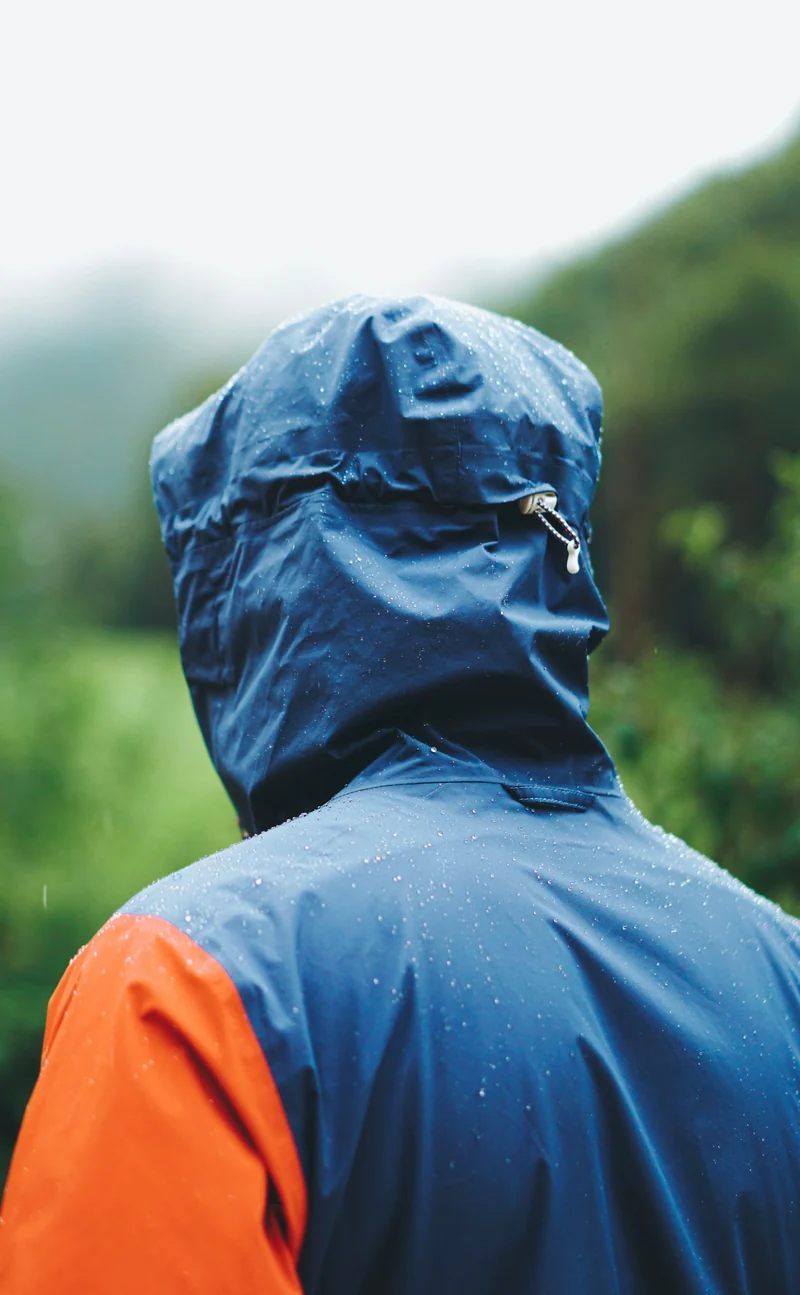 Hiker in a blue and orange hooded rain jacket from behind (demo photo)