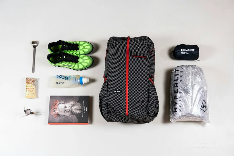 Trail kit laid out flat: backpack, shoes, shell and small gear (demo photo)
