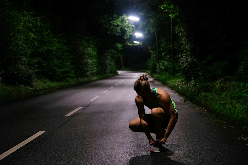 Runner crouching to tie a shoe on a dark road at night (demo photo)