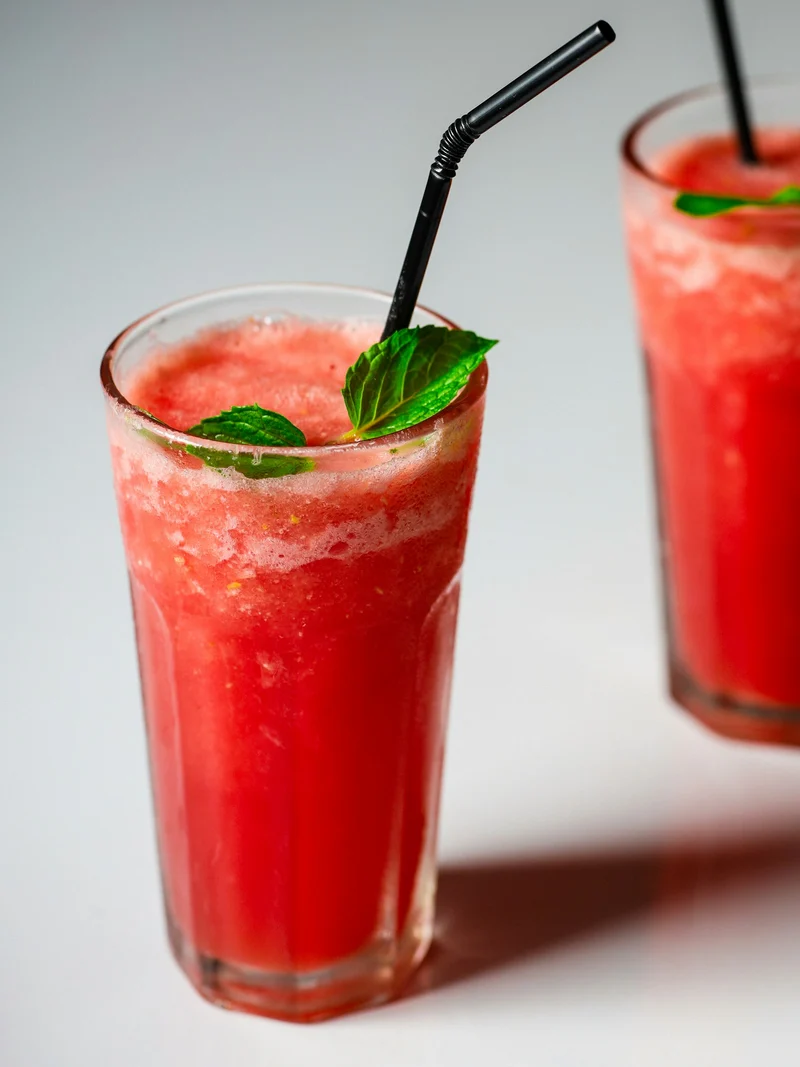 Two glasses of a red watermelon drink with mint and black straws (demo photo)