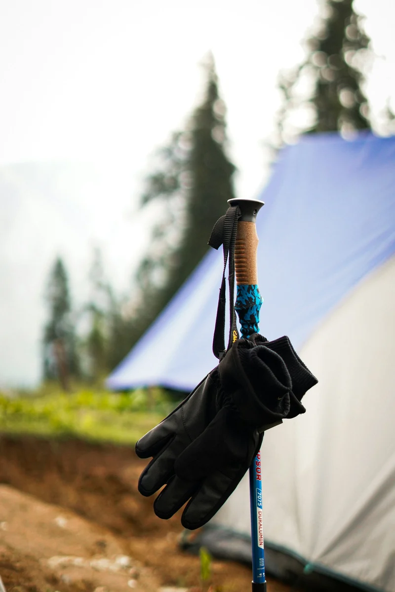 Black gloves hanging on a trekking pole beside a tent on a trail (demo photo)