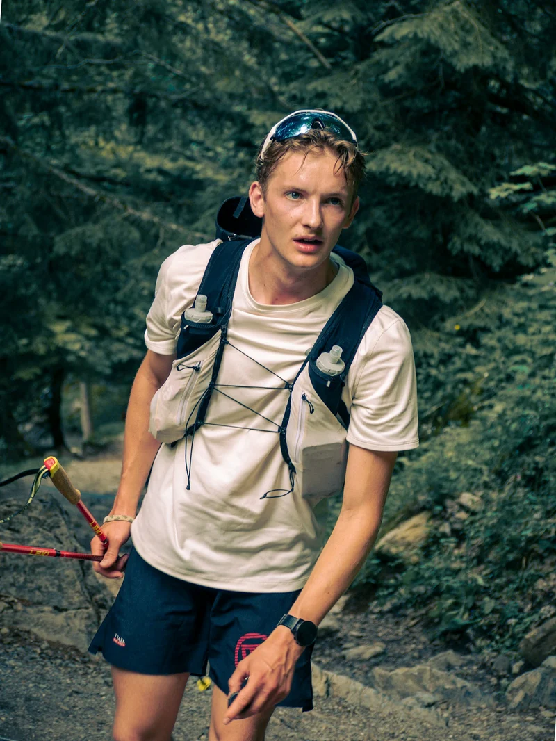 Trail runner wearing a hydration vest and holding trekking poles in a forest (demo photo)